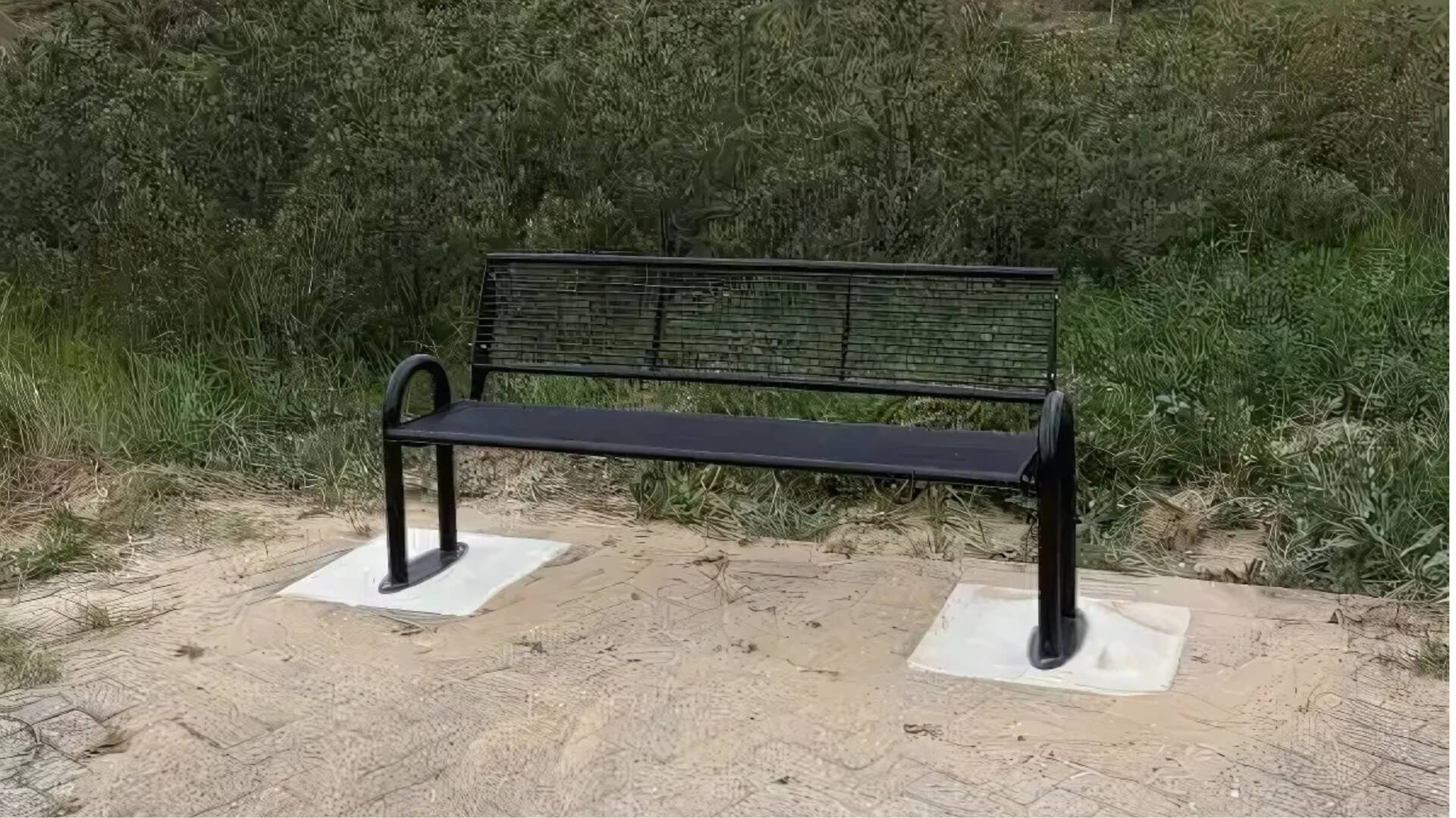 Zwarte stalen buitenbank met rugleuning en armleuningen, geplaatst op bestrating tussen gras en zand