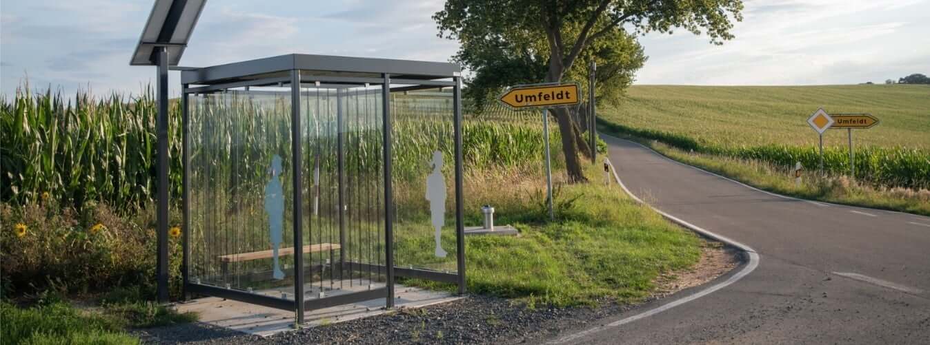 Bushokje geplaatst langs een landelijke gebied met een bord die in de richting van Umfeldt wijst.