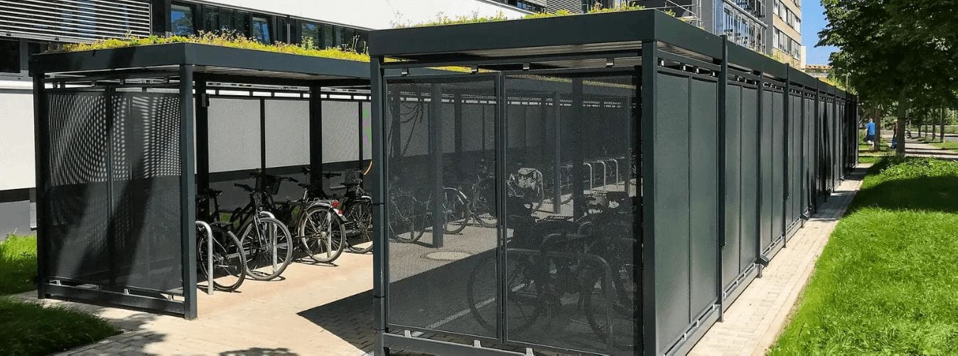 Fietsoverkapping met sedumdak en gesloten wanden voor veilige fietsenstalling geplaatst bij een kantoorgebouw.