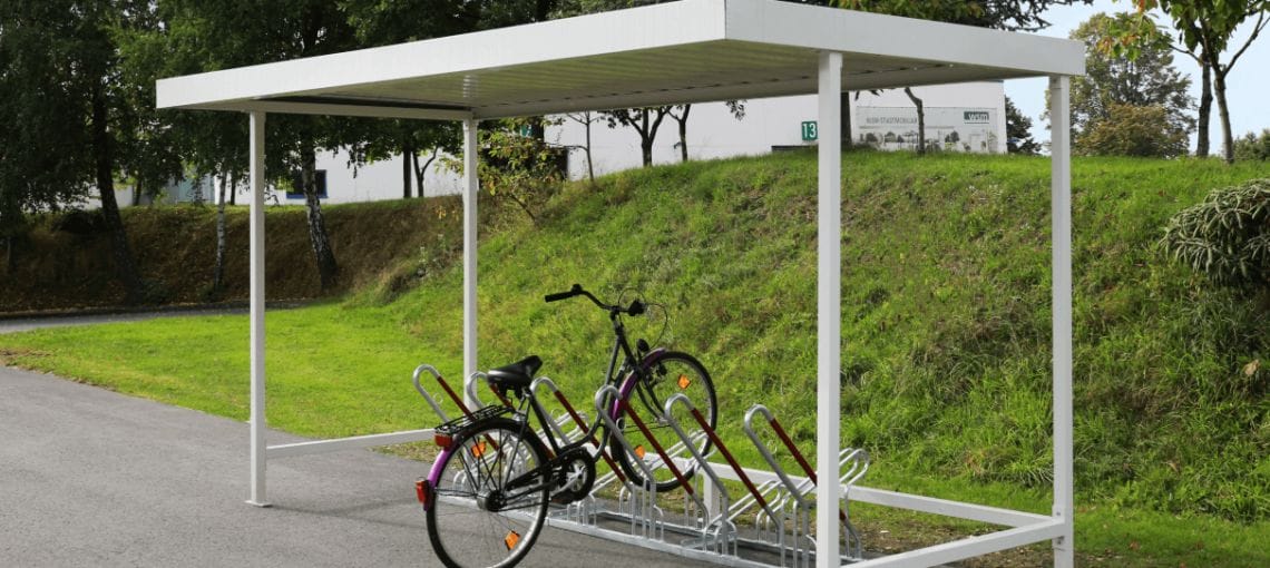 Bouwpakket Fietsoverkapping RAL-9002 met fietsenrekken, geplaatst op asfalt naast een grashelling.