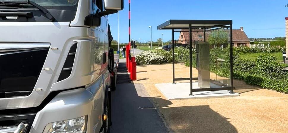 Betaalautomaat overkapping met een strak zwart stalen frame en transparante wanden, geplaatst naast een rijweg waar een vrachtwagen staat.