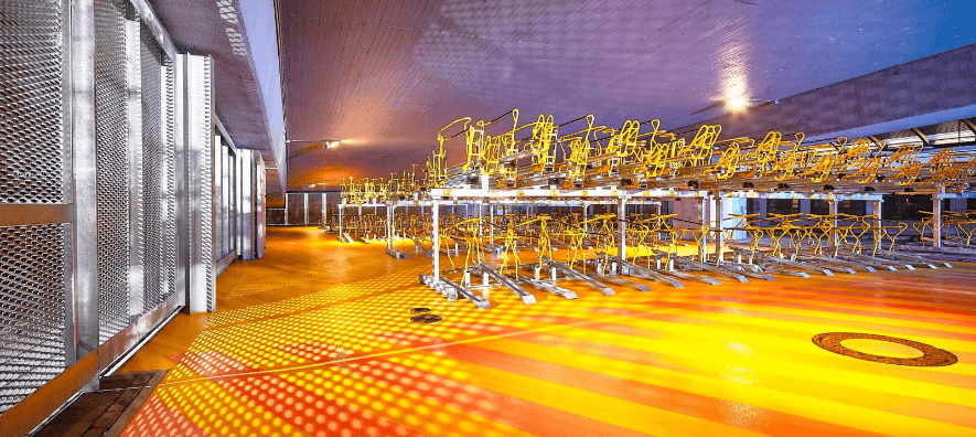 Binnenruimte met kleurrijke vloer en dubbellaags fietsenrek met gele beugels, geschikt voor het efficiënt stallen van fietsen op twee niveaus.