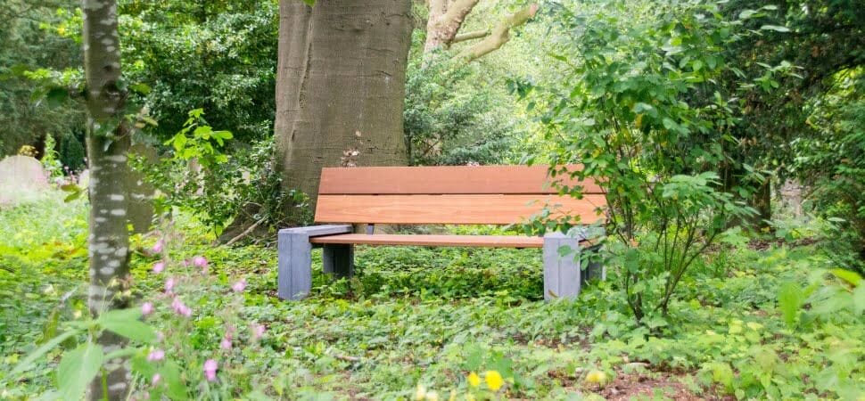 Parkbank ingezet als buitenbank van beton en gerecycled hout, geplaatst tussen bomen in een bos.
