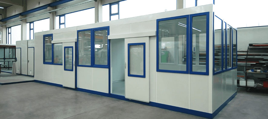 Prefab kantoorunit voor buiten met witte wanden, blauwe kozijnen en een schuifdeur met raam. De unit staat in een hal maar is ontworpen voor plaatsing in de buitenruimte.