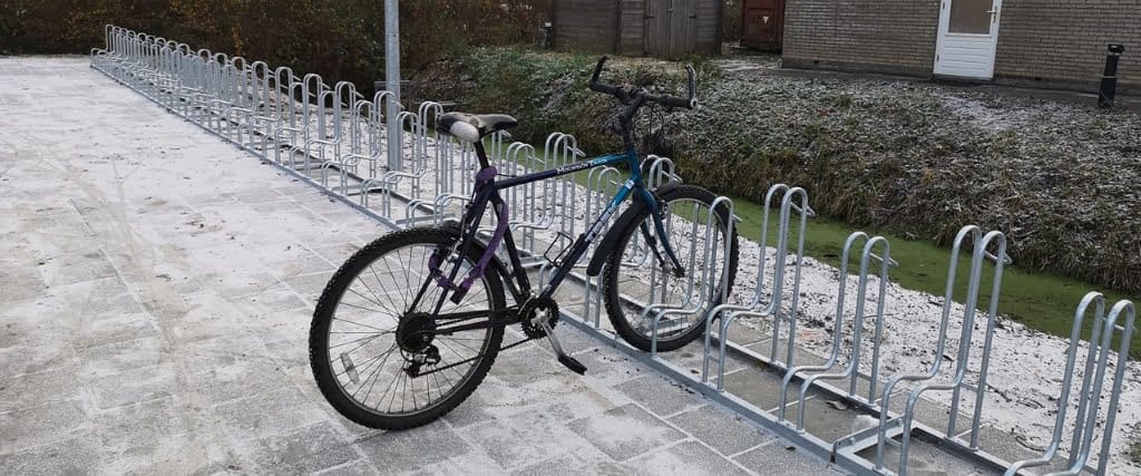 Lange rij fietsenrekken van verzinkt staal, geplaatst op bestrating met een fiets erin, bij HS88 in Hoogezand.