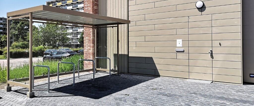 Compacte overdekte fietsoverkpaping met glaswanden, metalen frame en fietsaanleunbeugels geleverd aan een voedselbank in Almere