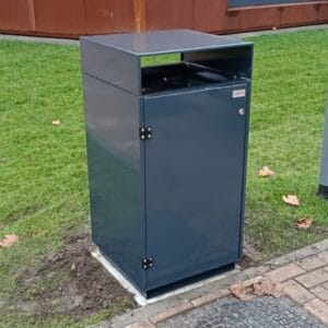 Donkergrijze buitenafvalbak van verzinkt staal met boveninworp, geplaatst op een betonnen voet langs een grasveld bij Reggesteyn in Nijverdal. De bak is afgewerkt in RAL 7016 en staat bij een modern schoolgebouw.