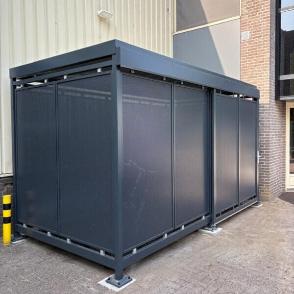 Gesloten fietsenberging van staal kopen Gesloten fietsoverkapping met geperforeerde stalen wanden en stalen frame in RAL-kleur, geplaatst tegen gevel.