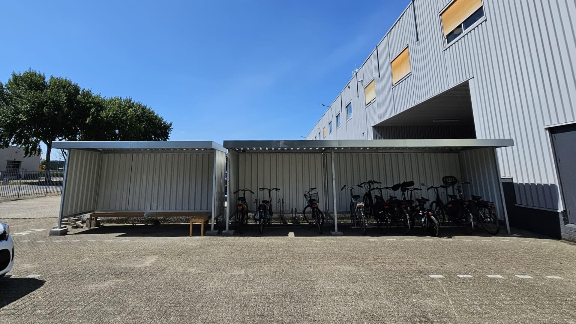 Fietsoverkapping en rookruimte van staal met zijwanden, geplaatst bij een bedrijfsgebouw.