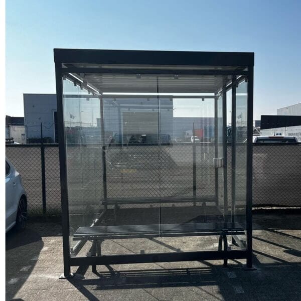 Rookabri van staal in ral-7016, voorzien 2 parkbanken en geplaatst op tegels van een parkeerplaats.