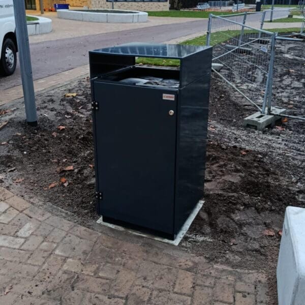 Afvalbak buiten bestellen voor onderwijsinstellingen Strak vormgegeven buitenafvalbak van verzinkt staal in RAL 7016, geplaatst naast een fietspad bij school Reggesteyn in Nijverdal. De afvalbak is stevig verankerd en ontworpen voor gebruik in de openbare ruimte.