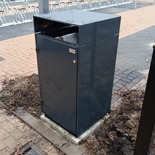 Afvalbak buiten bestellen voor schoolplein of fietsenstalling Donkergrijze afvalbak van verzinkt staal met boveninworp, geplaatst bij de fietsenstalling op het terrein van Reggesteyn in Nijverdal. De afvalbak is gemonteerd op een betonnen fundering en afgewerkt in kleur RAL 7016.