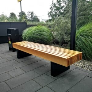 Moderne houten buitenbank zonder rugleuning, geplaatst in een groene buitenruimte met strakke bestrating.