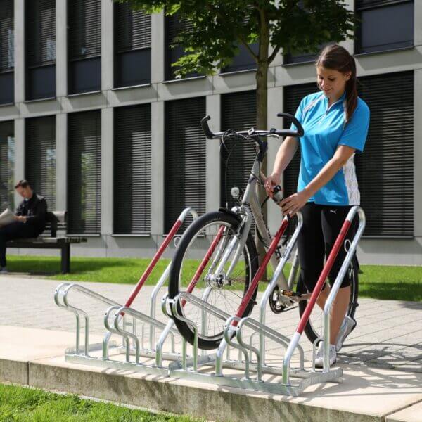 fietsenrek met valbeugel kopen Hoog-laag fietsenrek voor 4 fietsen met rode anti-kras valbeugels en slotoog, geplaatst voor een fietswinkel.