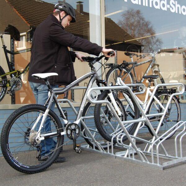 Verzinkte fietsenrek kopen Man parkeert fiets in verzinkt fietsenrek met valbeugel bij winkel
