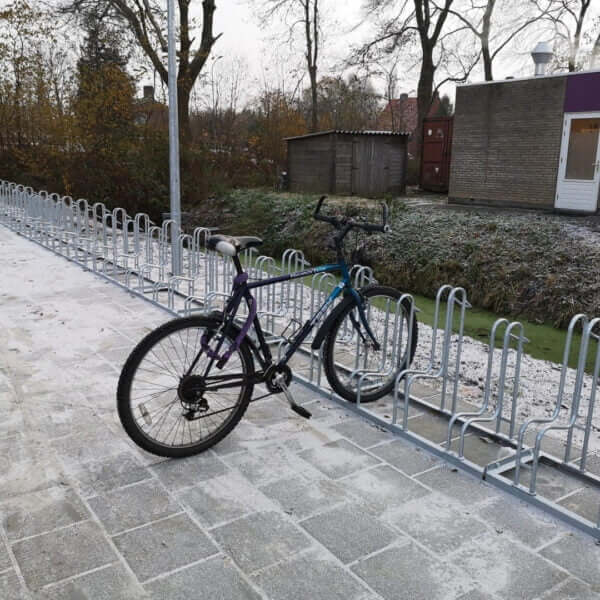 fietsenrek-online-bestellen Verzinkte fietsenrekken met fiets geplaatst op stoeptegels bij sportaccommodatie