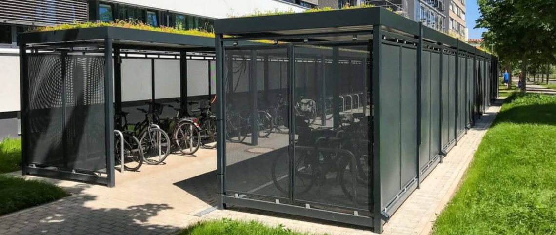 Stalen fietsoverkapping met sedum dak in kleur RAL-7016, met daarin fietsen en geplaatst naast een kantorengebouw. 
