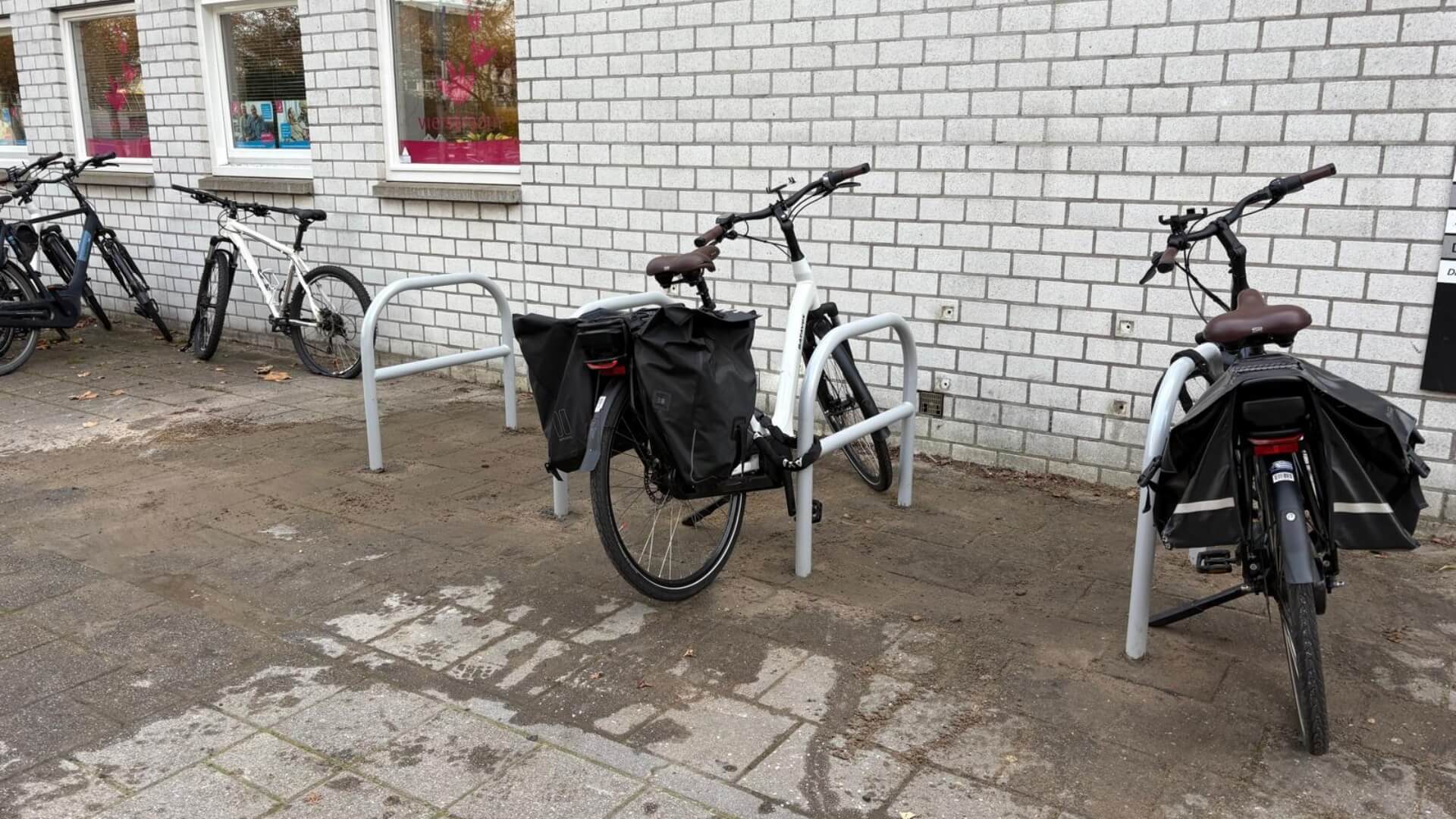 Zes fietsnietjes van verzinkt en gepoedercoat staal (RAL-9006) geplaatst bij Gezondheidscentrum de Watertoren in Zoetermeer. Twee fietsen staan geparkeerd aan de beugels met behulp van de tussenbuis, die het vastzetten van fietsen vergemakkelijkt.