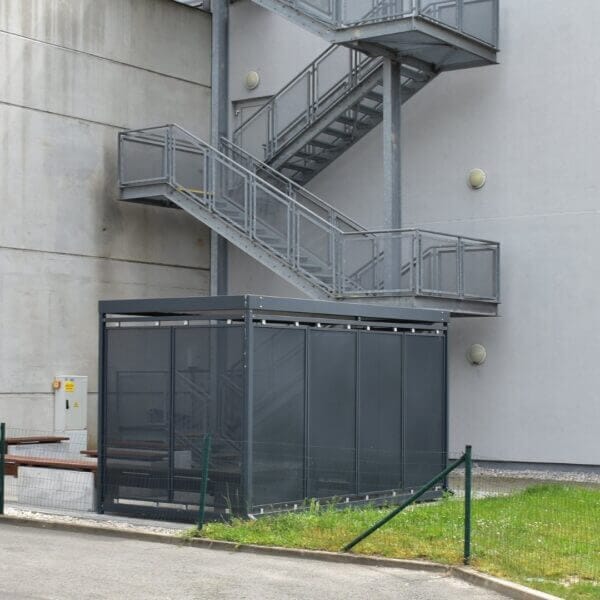 Rookabri voor bedrijfsrookbeleid Rookabri naast een bedrijfsgebouw met rookbeleid, voorzien van donkere glazen wanden en stalen constructie.