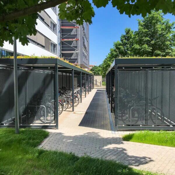 Ruime dubbele fietsoverkapping met geperforeerde wanden en sedumdak, voorzien van fietsnietjes voor veilige stallingsmogelijkheden.