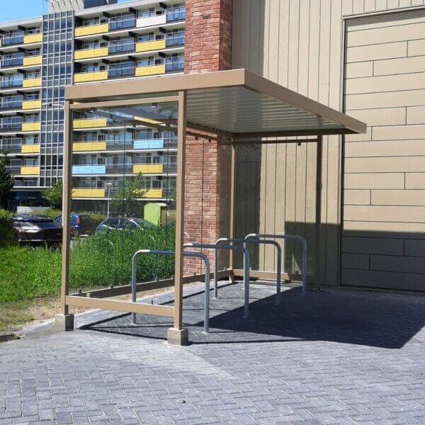 Fietsoverkapping in dezelfde kleur als het gebouw de Voedselbank met fietsnietjes voor veilige fietsenstalling.