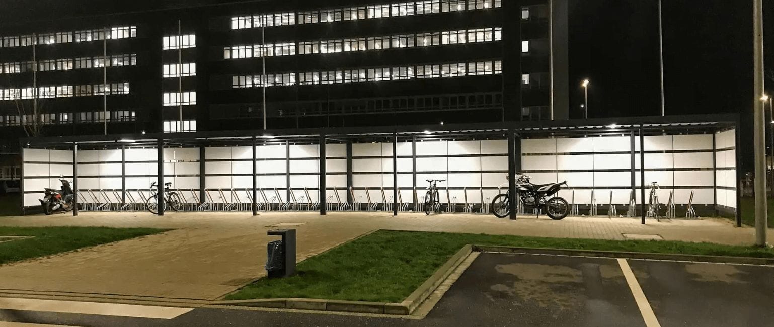 Fietsenstalling van staal en glas met LED-verlichting en fietsenrekken, geplaats en verankerd bij een VVE.