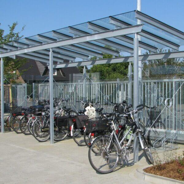 Verzinkte fietsoverkapping met glashelder dak en fietsenrekken eronder.