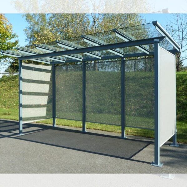 Multifunctionele fietsoverkapping met stalen wanden aanschaffen Fietsoverkapping met geperforeerde stalen zij- en achterwanden, dak van gehard glas in RAL-7016, verankerd op asfalt.