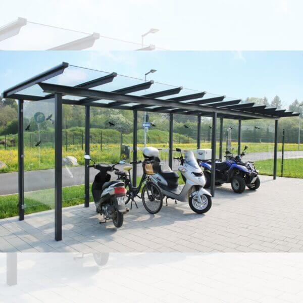 Multifunctionele fietsoverkapping met glazen dak en zijwanden Overdekte stalling met glazen dak en wanden, geschikt voor fietsen, scooters en brommers, geplaatst op een bestrate ondergrond in een groene omgeving.