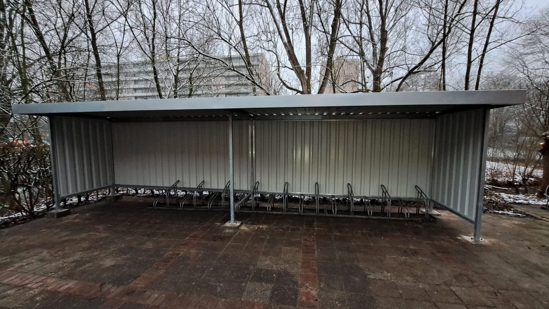 Overdekte stalen fietsenstalling met fietsenrekken, geplaatst op een bedrijventerrein en is alleen online te bestellen voor bedrijven en openbare ruimtes.
