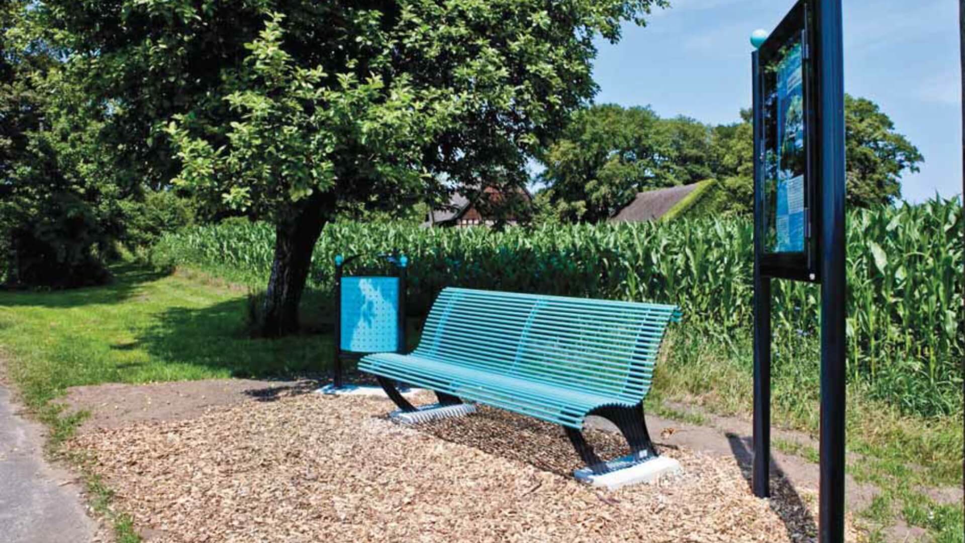 Parkbank van metaal geplaatst in een landelijke omgeving met een afvalbak voor buiten in zelfde kleur