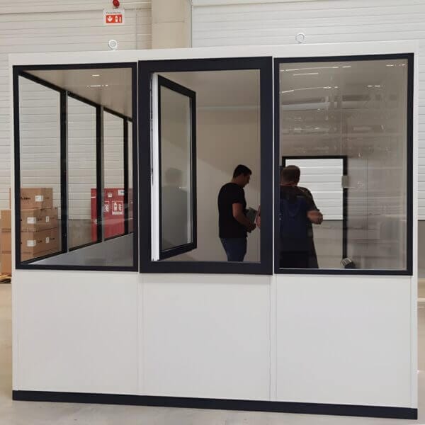 Modulaire Kantoorunit Direct Kopen Modulaire kantoorunit voorzien van veel ramen en geplaatst in een hal, in de kantoorunit staan 2 personen