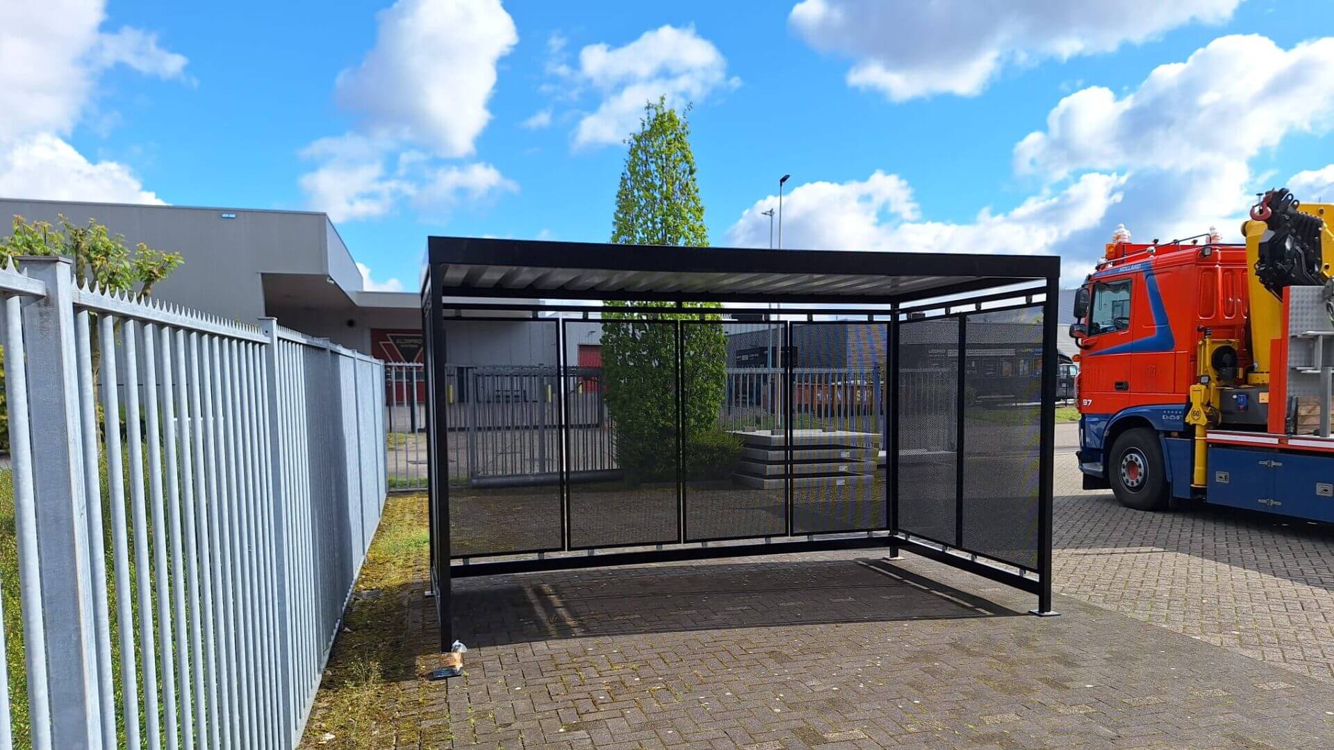 Fietsoverkapping van 4x2 meter voor stallen van fietsen, met stalen frame en geperforeerde stalen wanden, geplaatst op een nieuwbouw bedrijfsterrein