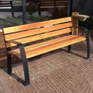 Houten seniorenbank met zwart stalen frame op een ondergrond van straatklinkers.