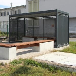 Rookabri met wanden van geperforeerd staal in RAL 7016 en optionele zitbanken van hout op betonnen fundering.