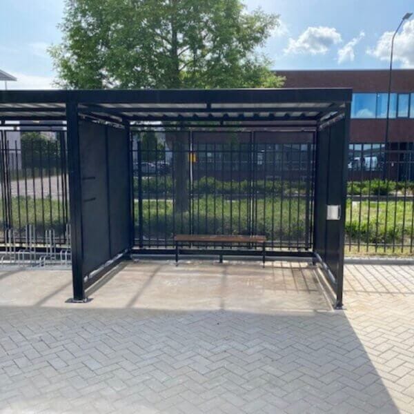 Zwarte rookabri met zitbank en wandasbak kopen Compacte rookoverkapping met gesloten stalen zijwanden, zitbank en wandasbak, zwart gepoedercoat en geplaatst op klinkerbestrating.