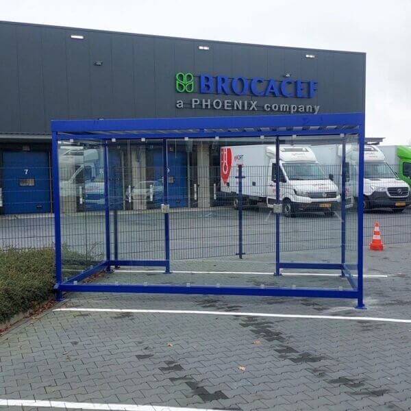Rookoverkapping voor buiten geplaatst op terrein Brocacef Blauwe rookoverkapping met glazen wanden, geplaatst op het terrein van Brocacef naast bedrijfswagens.