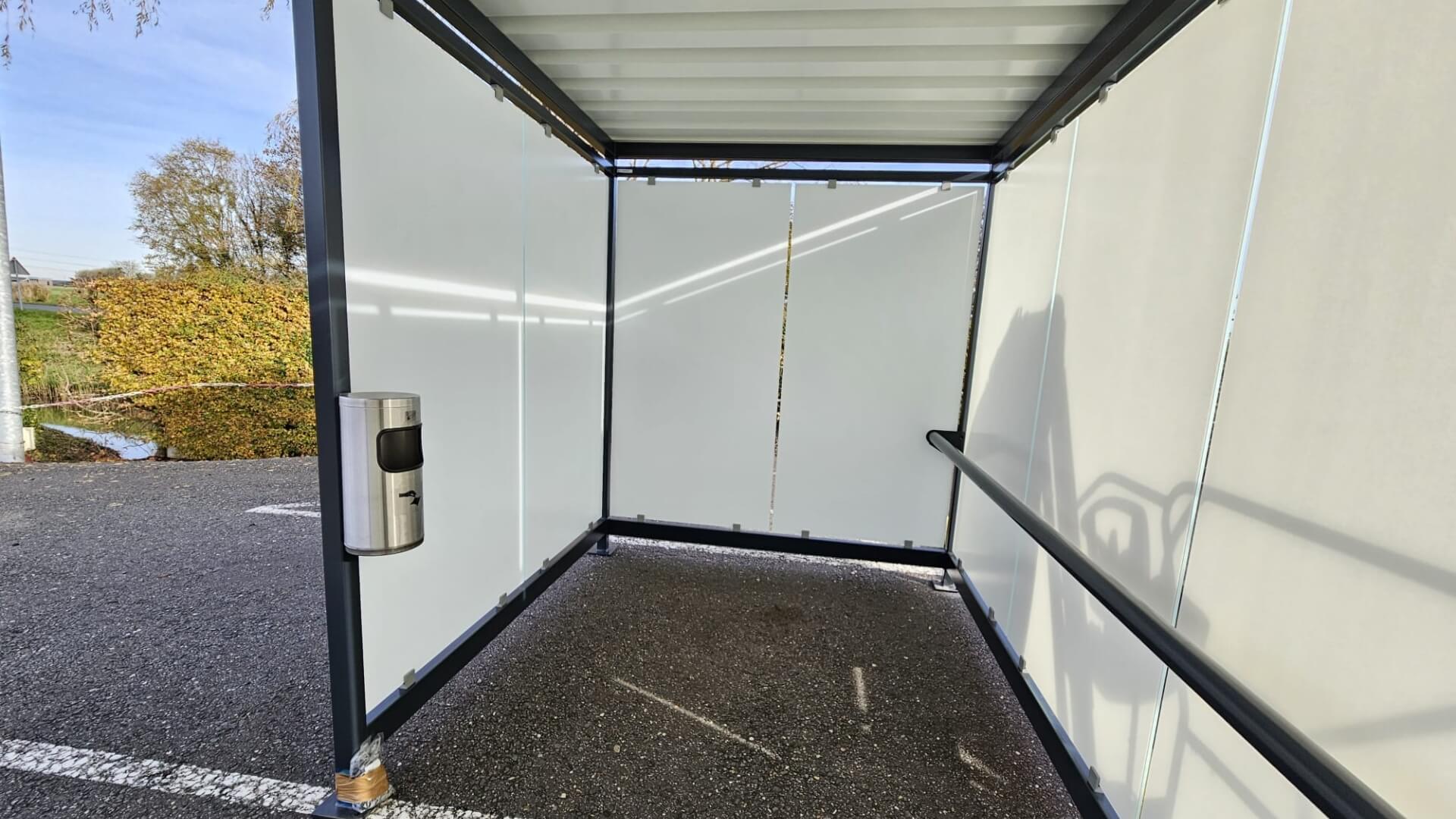 Binnenkant van een rookabri van Umfeldt bij FrieslandCampina in Bedum, voorzien van glazen wanden met zeefdruk, leunbeugel en wandasbak met afvalbak.