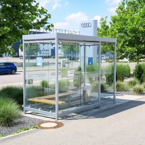 Grijze rookhok direct online bestellen Grijze rookoverkapping met glazen wanden, optionele zitbank en buitenasbakken, geplaatst bij Audi.