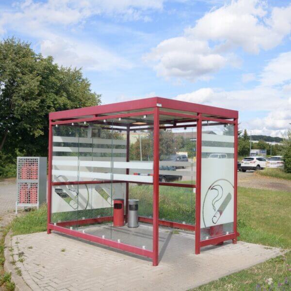 Rode rookoverkapping buiten kopen Rode rookoverkapping met glazen wanden voorzien van zeefdruk en rookpictogrammen, geplaatst op bestrating in een buitenomgeving.
