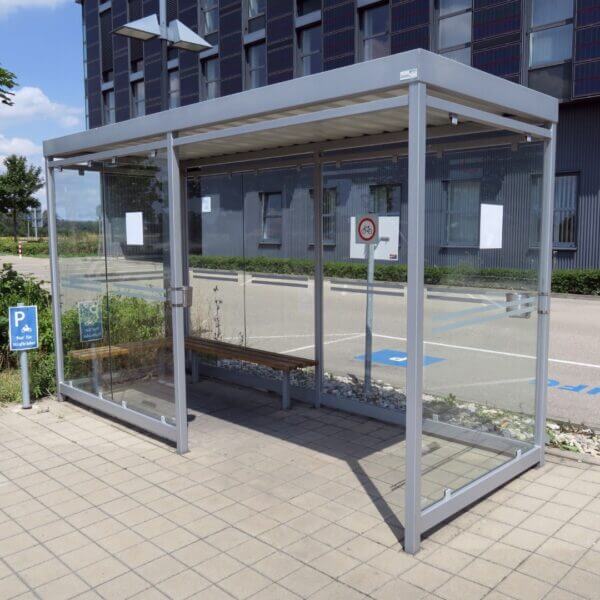 Grijze rookabri met ESG glazen wanden en stalen frame, optioneel voorzien van een wandasbak gemonteerd aan de staander, leverbaar in diverse RAL-kleuren.
