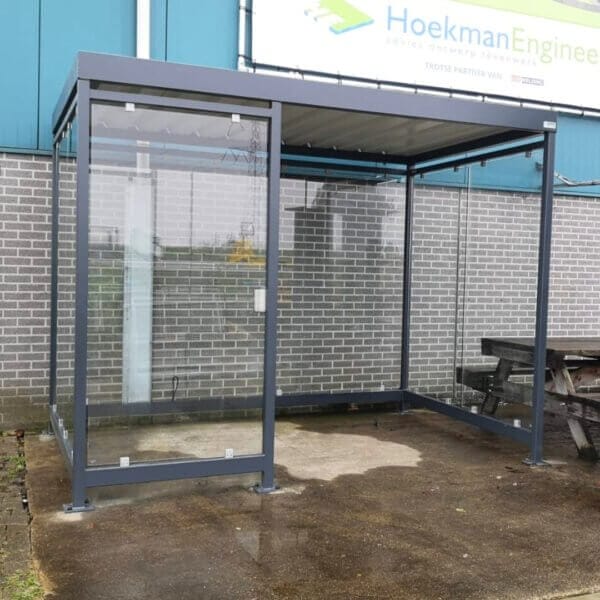 Rookcabine online aanschaffen Rookcabine met glazen wanden en stevig metalen frame, verankerd op beton en voorzien van een optionele wandasbak.