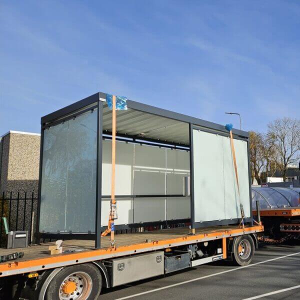 Rookabri prefab kopen Rookabri met glazen wanden en metalen dak op een vrachtwagen, klaar voor installatie als rookvoorziening buiten.
