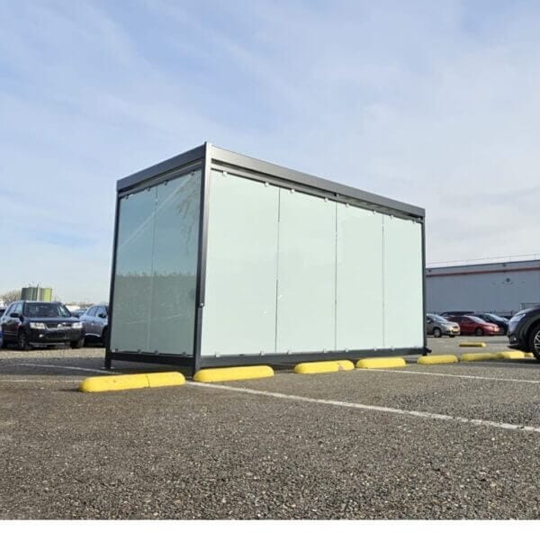 Rookoverkapping 4x2 meter met zeefdrukglas kopen Rookoverkapping van 4x2 meter met glazen wanden voorzien van zeefdruk, geplaatst op een parkeerplaats tussen geparkeerde auto's.