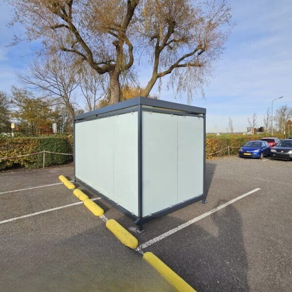 Rookoverkapping van Umfeldt direct aanschaffen Rookoverkapping met matte glazen wanden en stalen frame, geplaatst op een parkeerplaats naast enkele auto's.