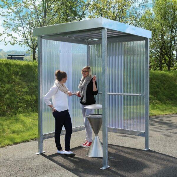 Verzinkte rookabri met polycarbonaat zij- en achterwanden, twee personen rokend bij een asbak