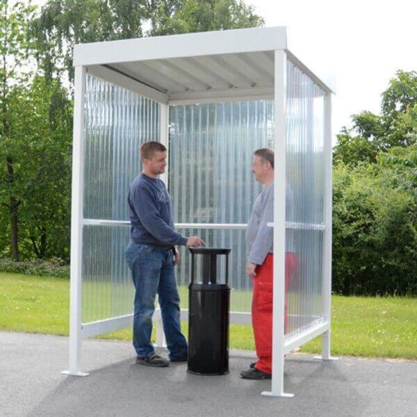 Rokersabri aanschaffen voor bedrijventerreinen Rookabri gepoedercoat in RAL-9002 met polycarbonaat zij- en achterwanden, gebruikt door twee personen met een zwarte asbak