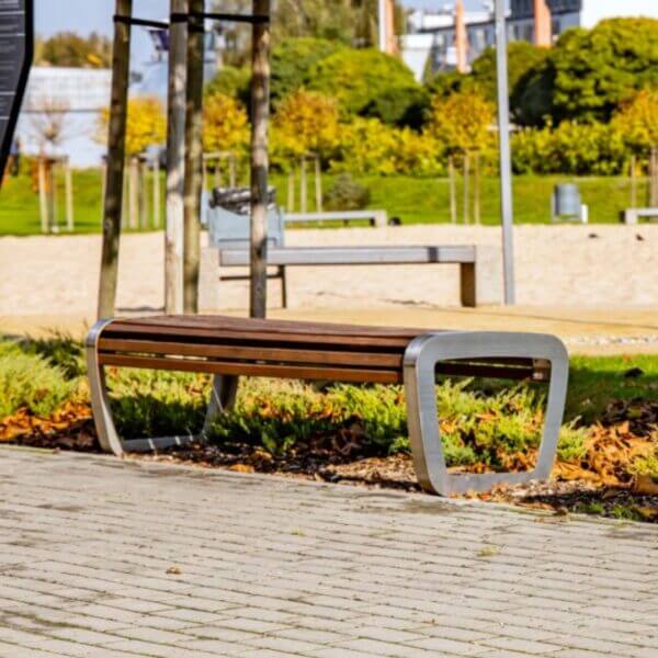 Moderne buitenbank met hardhouten zitting en RVS frame in een openbare ruimte met groen en bestrating.