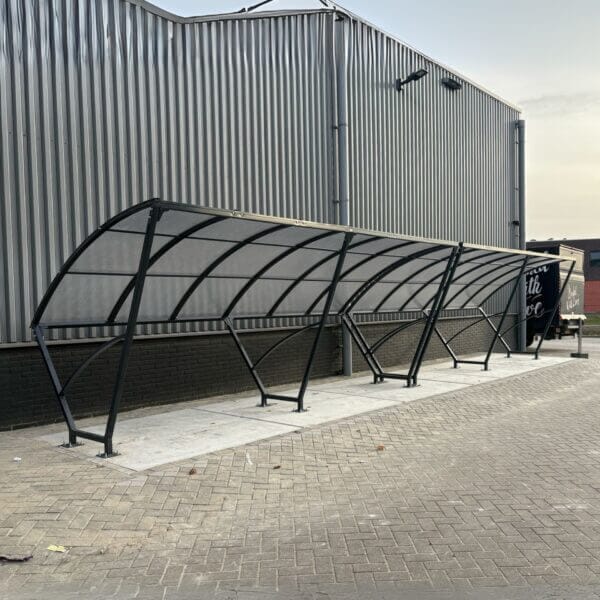 Fietsoverkapping 10 meter online bestellen voor bedrijven Fietsoverkapping van 2 x 5 meter in kleur zwart, van staal en polycarbonaat geplaatst op beton.