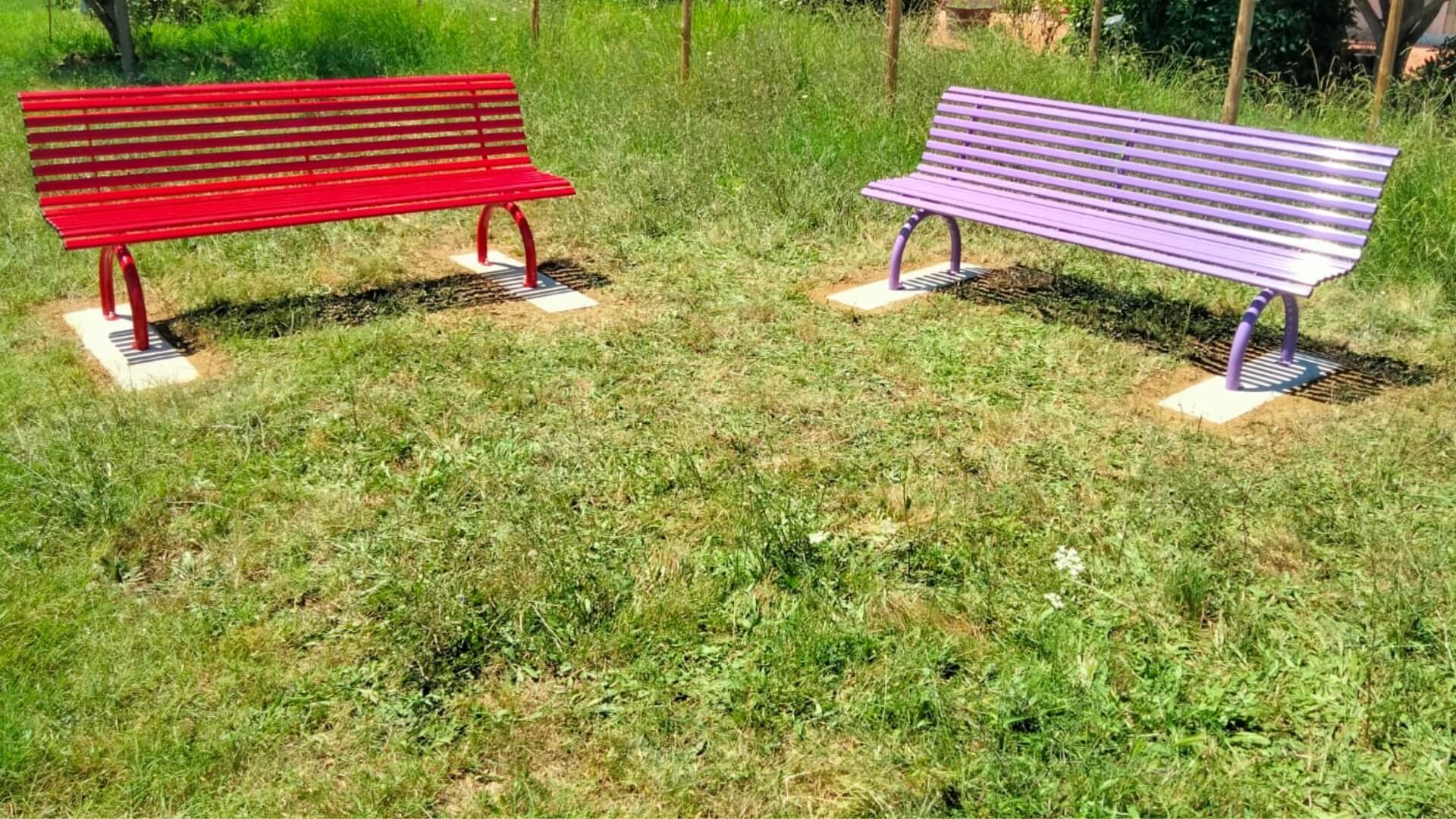 2 parkbanken geplaatst in gras, één heeft kleur rood en de ander paars